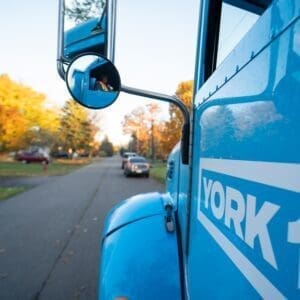 A cyan YORK1 truck delivering a dumpster bin.